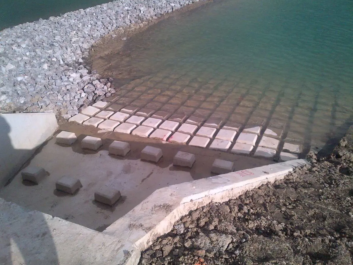 Su kenarında beton blok apron ve kırma taş (riprap) çıkış yapısı: yüksek hızlı akış enerjisini kırmak için düzenli dizilmiş precast beton bloklar ve çakıl dolgu