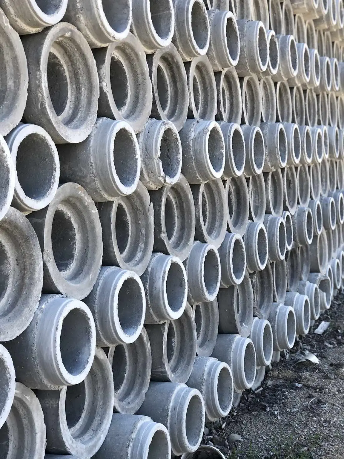 Saha stok alanında katman katman istiflenen çok sayıda dairesel beton boru elemanı; her borunun uçlarındaki soket ve spigot birleşim detayı görünmektedir