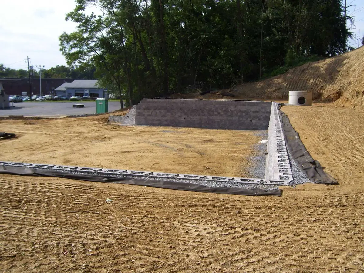 İstinat duvarı arkasında drenaj saha uygulaması — beton blok istinat duvarı önünde çakıl drenaj bandı ve geotekstil şerit döşeli, arka planda yuvarlak beton kontrol bacası