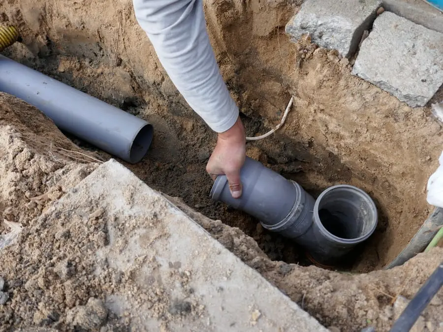 Kazı çukurunda gri PVC boru eki elle konumlandırılıyor — boru uç birleşim noktası yakın çekim
