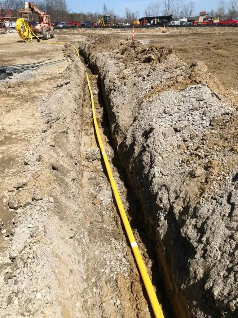 Açık hendekte döşenmiş sarı renkli doğal gaz PE borusu — uzun düz hendek çizgisi boyunca boru açık arazide serilmiş, arka planda iş makineleri