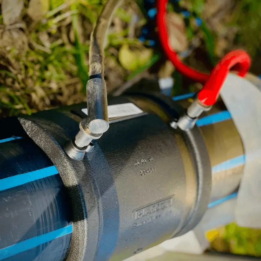 PE boru üzerinde elektrofüzyon manşonu kurulumu — siyah boru gövdesine oturan manşondan kırmızı ve mavi kablo çıkıyor, kaynak süreci devam ediyor