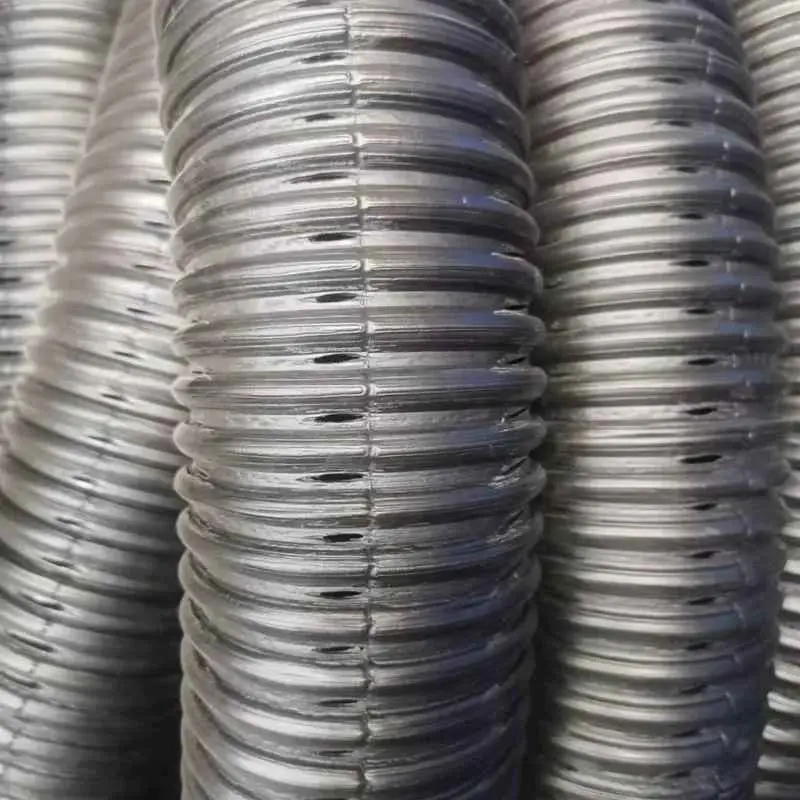 Gümüş/çelik renkli HDPE spiralli koruge drenaj borularının yakın çekim kesit görüntüsü: her boğumda oval şekilli delikler açıkça görülüyor; borular yanyana istifleniyor