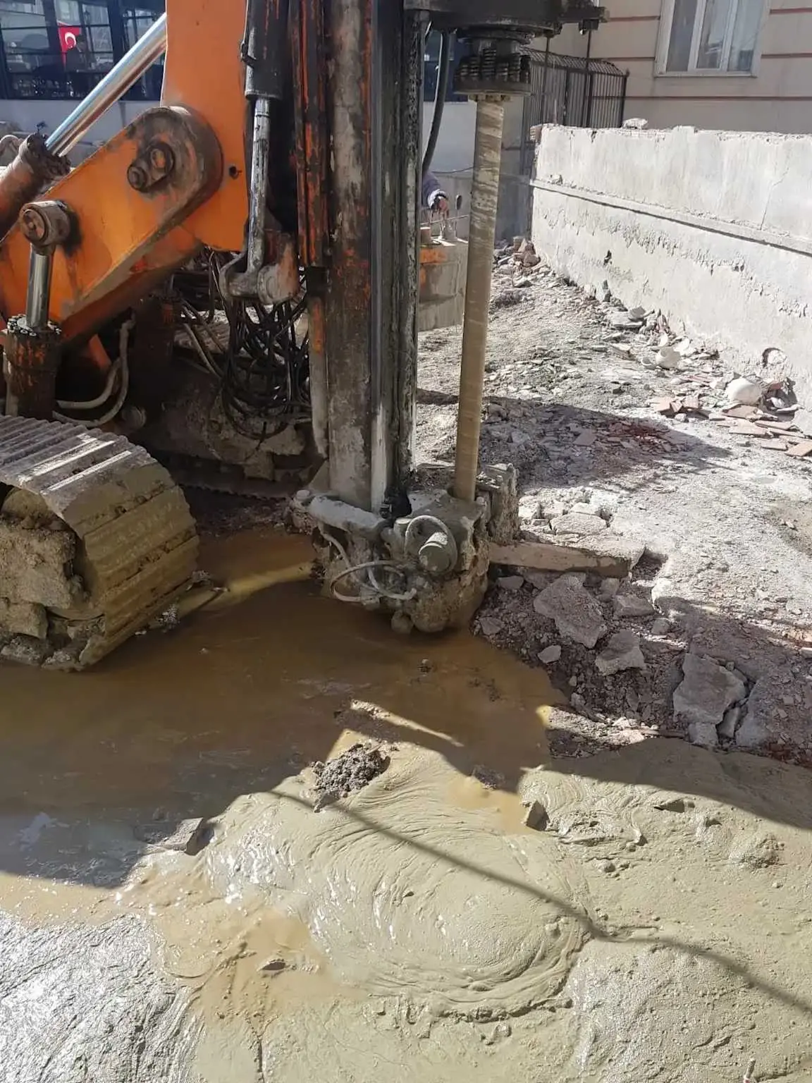 Şehir içi kazık delme makinesi çalışması — delgi matkabı ve çamurlu su boşalması, beton kaldırım zemininde sıkışık alan