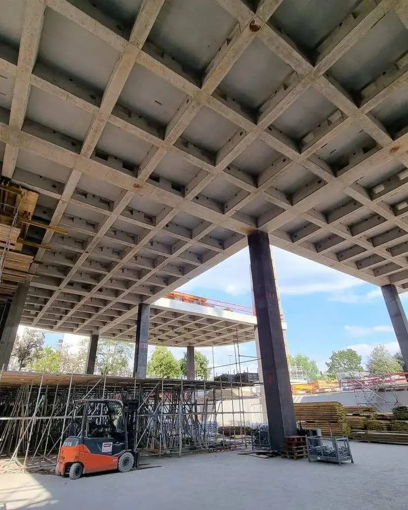 Kaset döşeme tavan alttan görünüm — dikdörtgen grid boşlukları, beton kirişler ve fork-lift inşaat şantiyesi