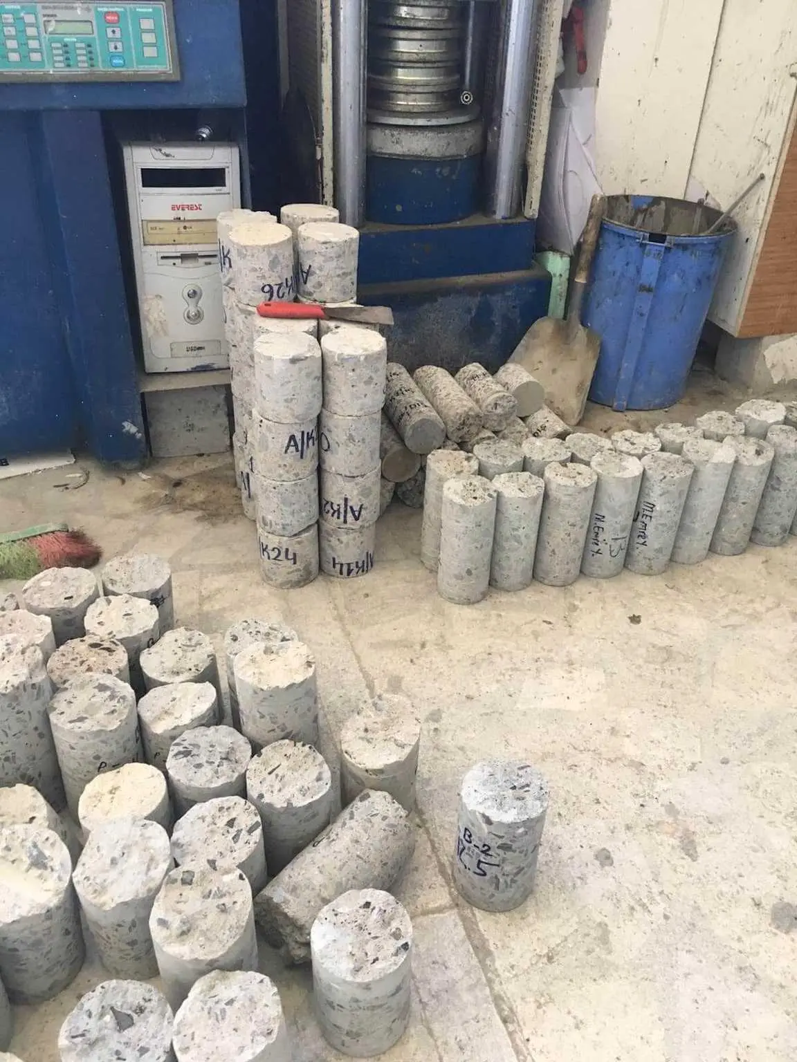 Laboratuvar zemininde gruplandırılmış çok sayıda silindirik beton karot numunesi — etiketli ve numaralı