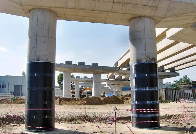 Köprü ayaklarına CFRP siyah kumaş sarma güçlendirmesi — iki silindirik beton kolon CFRP bantlarla çevrili