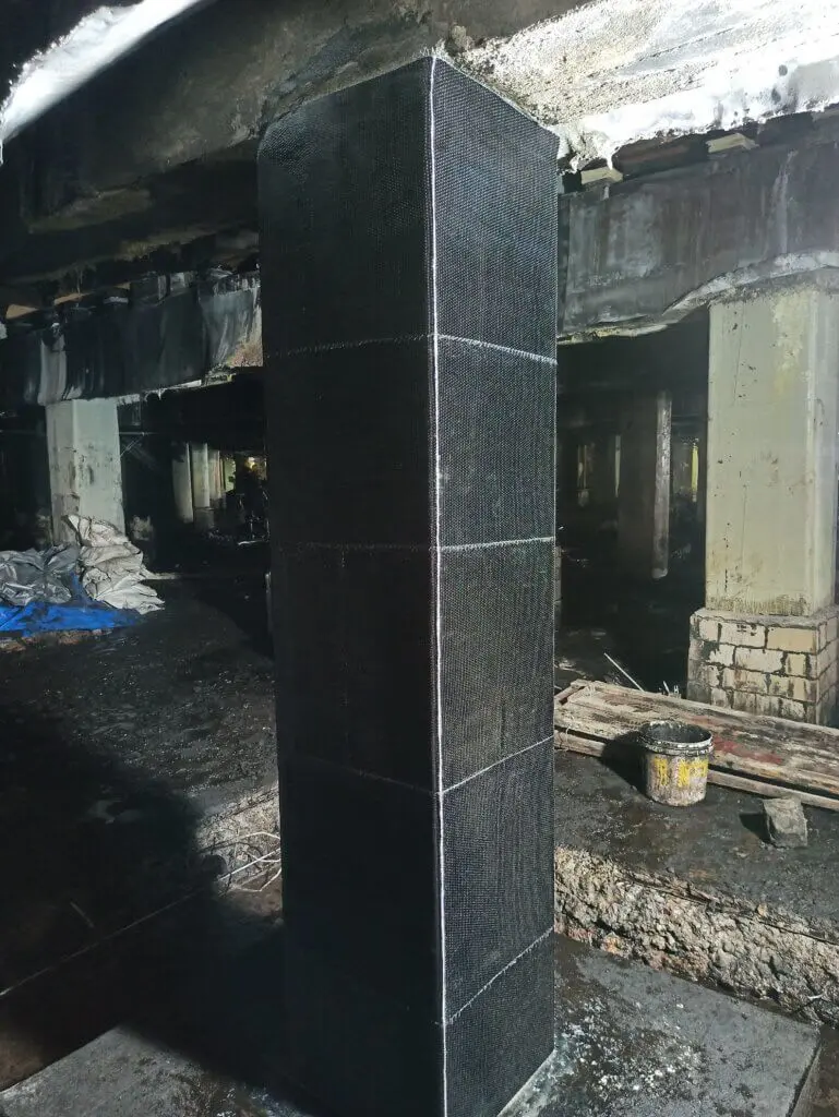 CFRP sargılı betonarme kolon iç mekân uygulaması — koyu siyah karbon fiber katmanlarla sarılmış kare kolon
