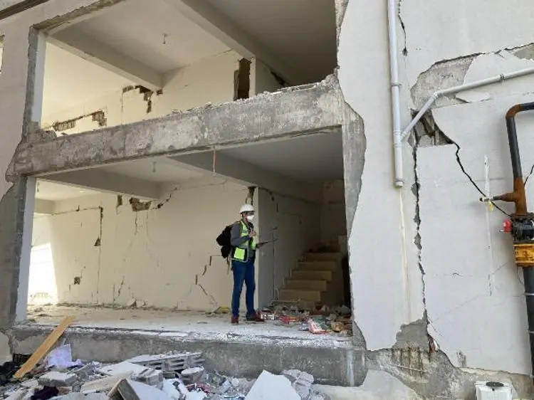 Deprem hasarı görmüş binada perde ve kolon hasarı: zemin katta perde tamamen çökmüş, İSG ekipmanı giyen bir mühendis enkaz içindeki zemin katı inceliyor