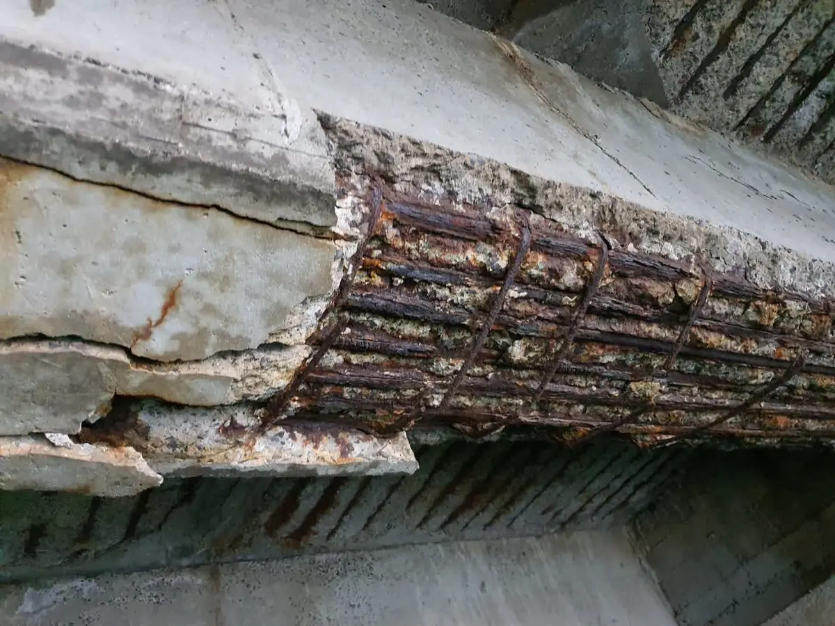Korozyon hasarı görmüş betonarme kiriş alt yüzeyi: beton örtüsünün tamamen soyulduğu ve paslanmış donatı çubuklarının açıkta kaldığı ileri derece çatlak ve korozyon hasarı