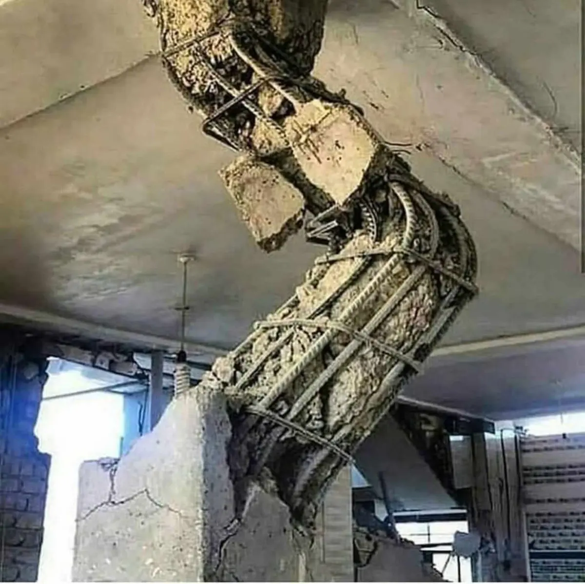 Narin kolon burkulmaya bağlı hasar fotoğrafı: beton örtüsü sıyrılmış, boyuna donatılar dışa fırlayarak spiral biçim almış, kiriş-kolon birleşim noktasında ciddi betondaki çökme görülüyor