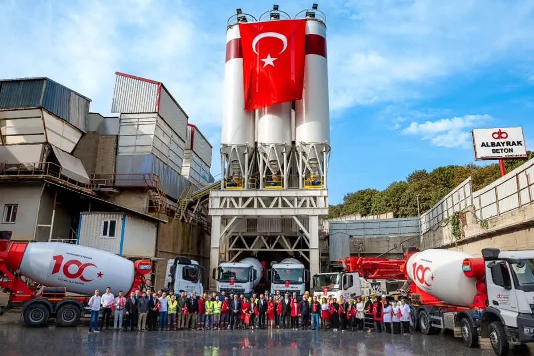 Albayrak Beton hazır beton santralinin cephe görünümü; ön planda mikserlerin sıralandığı, arkada siloların yer aldığı tesis, önünde çalışanlar ve Türk bayrağı ile birlikte gösterilmekte
