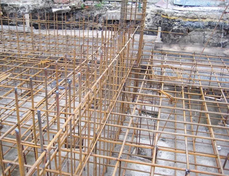 İnşaat şantiyesinde kalıp içine yerleştirilmiş ve beton dökümü bekleyen çok sayıda betonarme kolon ve kiriş donatısı iskeleti; donatı çubukları, etriyeleri ve bağlantı elemanları görünmekte
