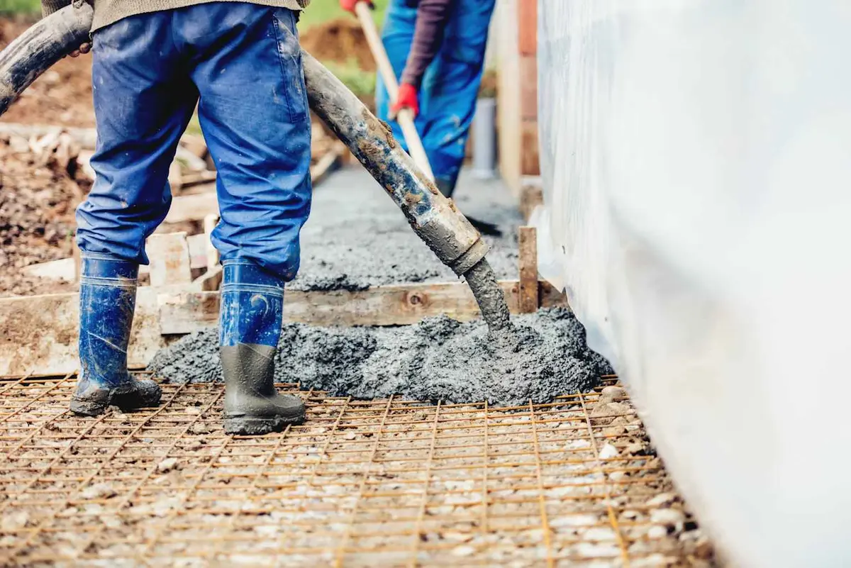 Şantiyede döşeme beton dökümü: işçiler hortumla C25/30 beton döküyor, altında donatı ağı görünür