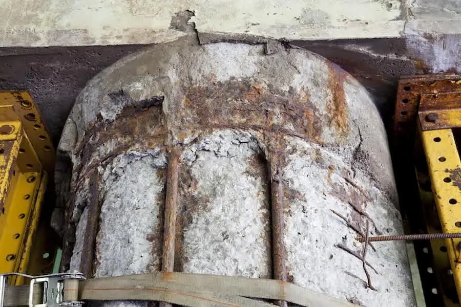 Şiddetli klorür korozyonuna uğramış betonarme kolon başlığı: beton yüzeyi tamamen dağılmış, donatı ve etriyeler beyazımtırak tuz birikmesiyle kapanmış, yoğun paslanma mevcut