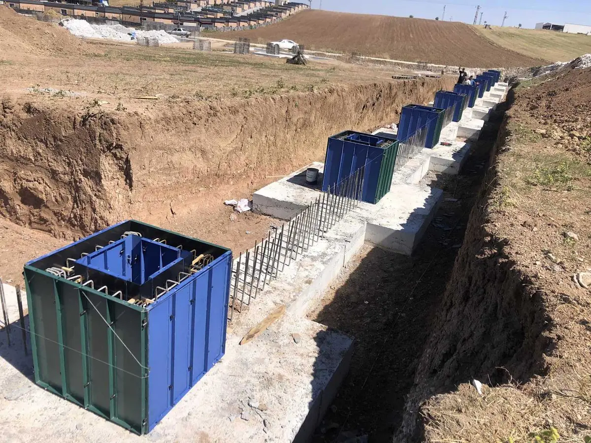 Prefabrik sanayi yapısı inşaat alanında mavi plastik soket kalıpları monte edilmiş betonarme temeller: soket boşlukları mavi renkli polipropilen kalıplarla belirlenmiş, soket etrafında çelik donatı görünüyor