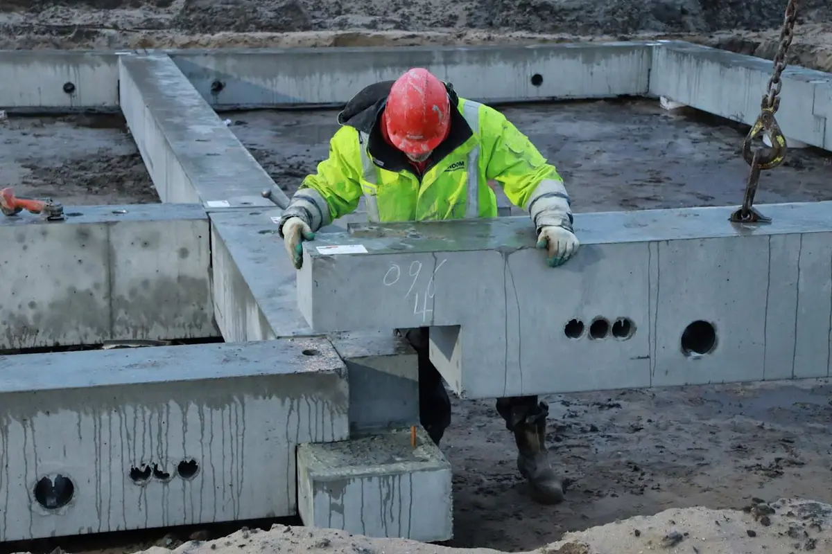 Şantiyede goblet tipi prefabrik betonarme kiriş ucu yerleştirme: işçi koruyucu ekipmanlarıyla kiriş ucunu goblet beton yüzeyine oturtarak montaj yapıyor; kiriş ucundaki kesme boşlukları görünüyor