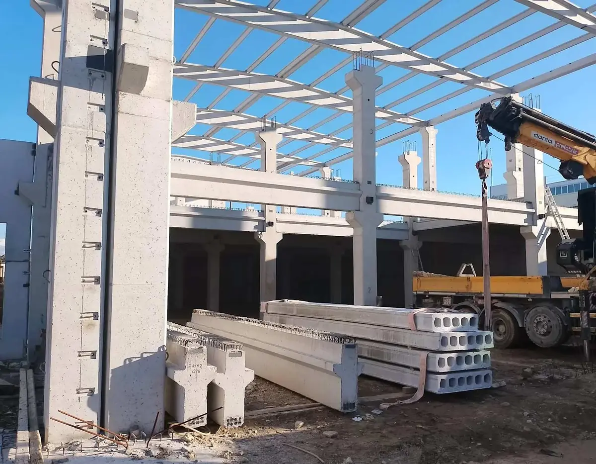 Prefabrik sanayi yapısı inşaat alanı: ön planda çift-T boşluklu döşeme plakaları, arkaplanda monte edilen prefabrik kolonlar ve kirişler