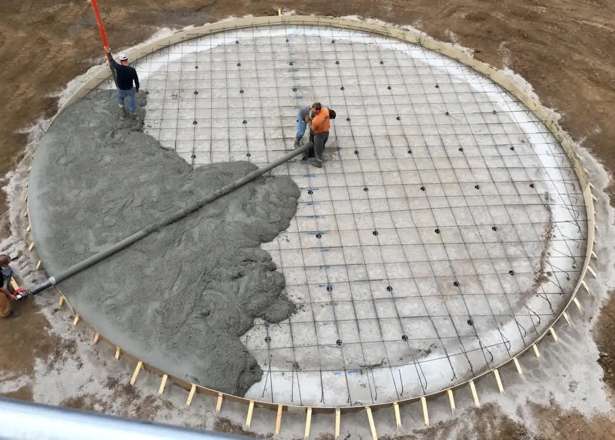 Silindirik betonarme depo taban döşemesi: dairesel halka donatı serimi tamamlanmış, beton dökümü başlamış; işçiler röperle yüzey tesviyesi yapıyor