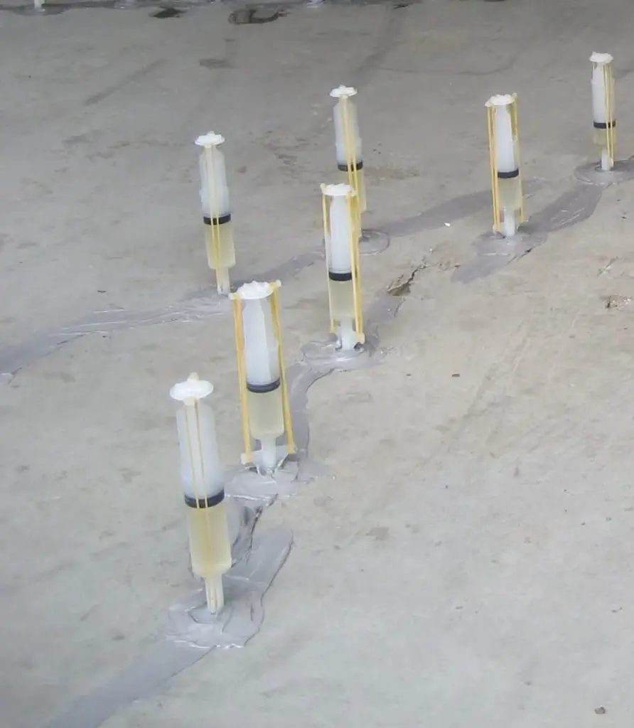 Epoksi enjeksiyon şırıngaları: beton döşeme yüzeyindeki çatlak boyunca yerleştirilmiş plastik şırınga enjektörler, epoksi sızıntısı görünüyor