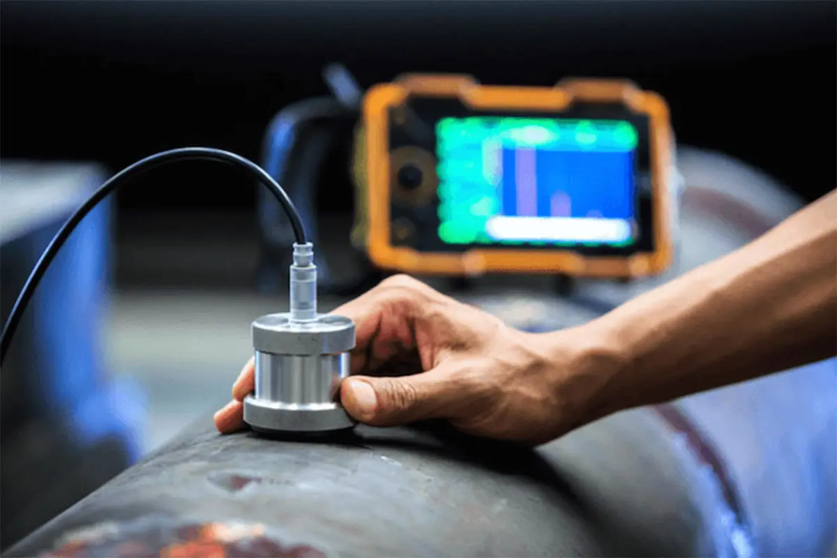 Ultrasonik NDT muayenesi — çelik boru üzerinde transdüser (prob) ve dijital A-tarama ultrasonik test cihazı ekranı, iç kusur tespiti