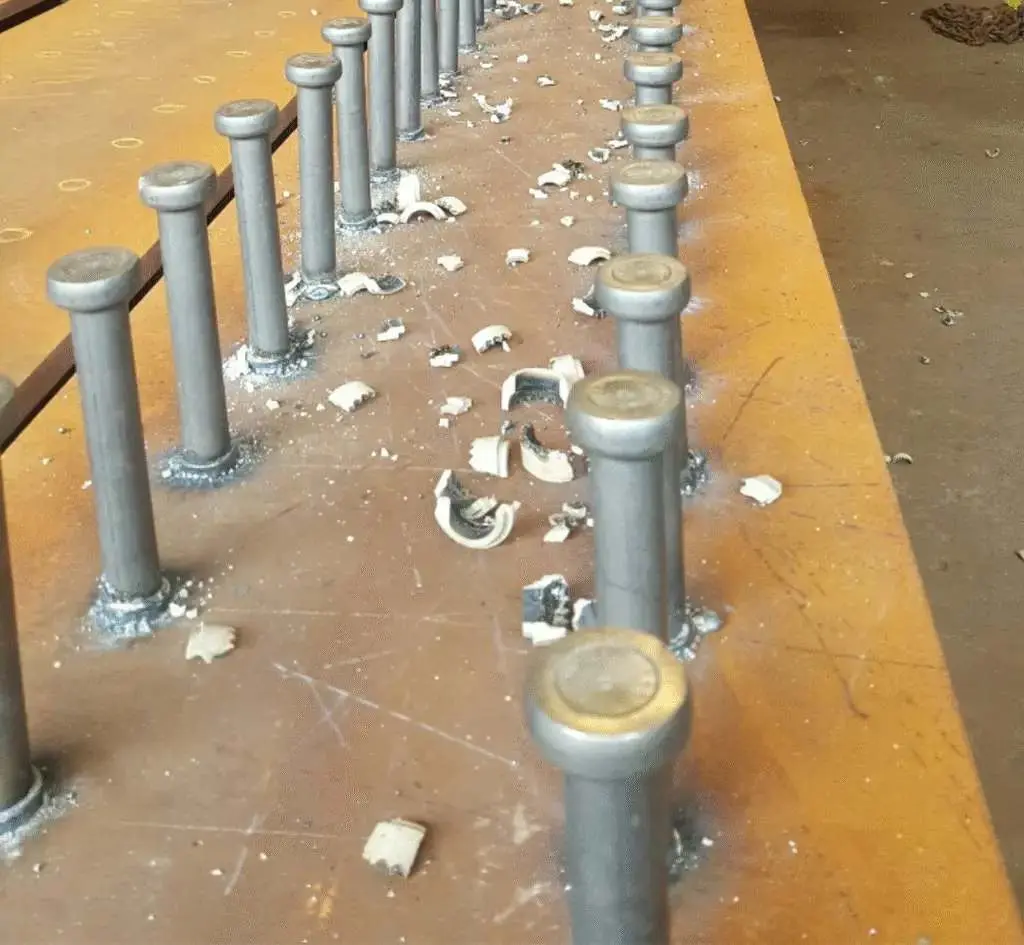 Çelik kiriş üst başlığına kaynak edilmiş stud çivileri — ark saplama kaynağı sonrası seramik halkalar kırık hâlde görünmekte; stud çivisi dizisi imalathane ortamında