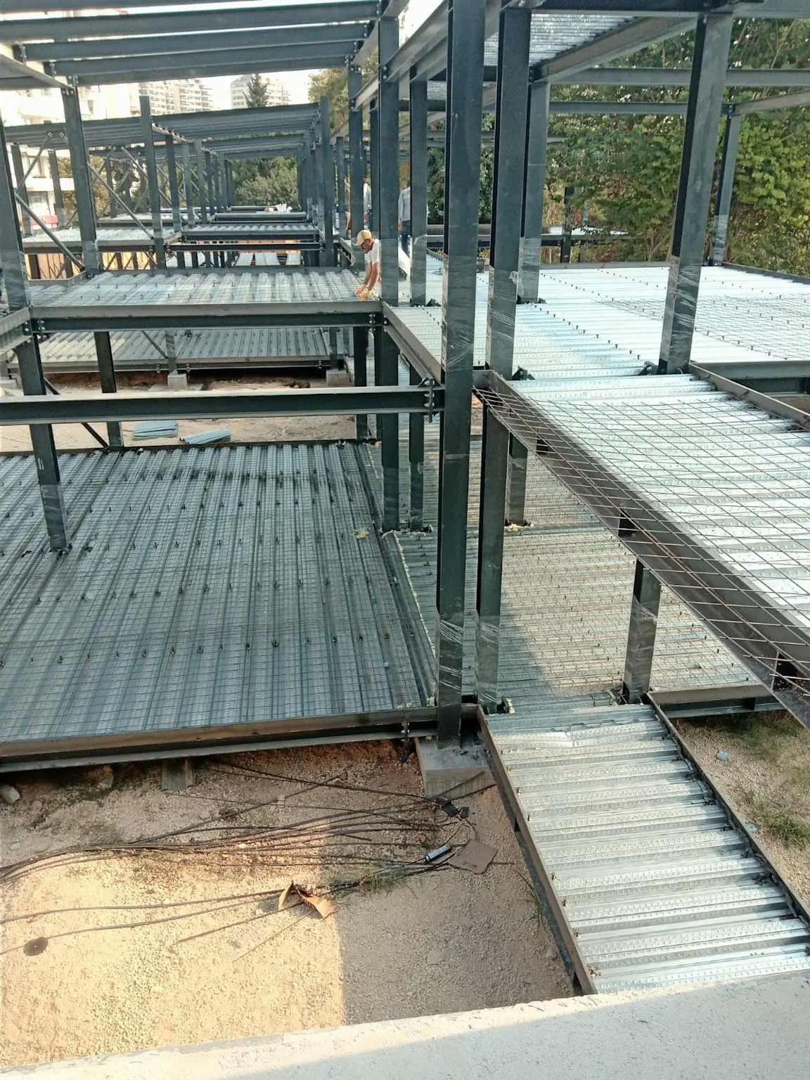 Çok katlı çelik yapıda trapez sac döşeme sistemi şantiye montajı: birden fazla kat seviyesinde galvanizli trapez sac döşemeler yerleştirilmiş, çelik iskelet tamamlanmış; Türkiye şantiye uygulaması