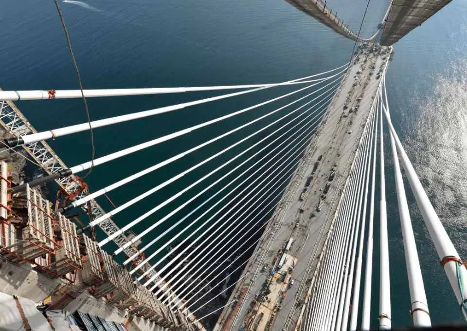 Yukarıdan bakış — pylon tepesinden eğik stay kablolar tabliyeye uzanıyor, deniz görünümü