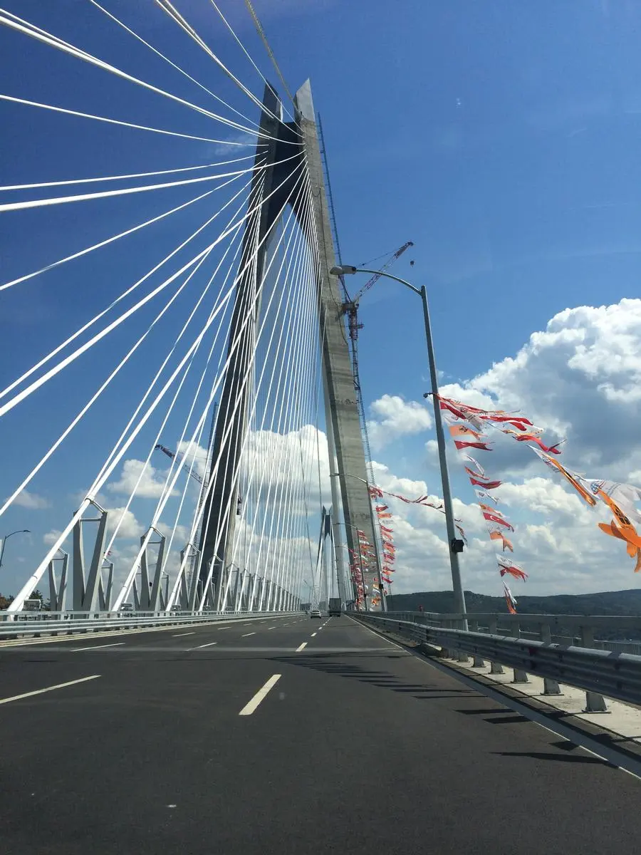 Yavuz Sultan Selim Köprüsü tabliyeden görünüm — beyaz stay kablolar ve beton pylon, açılış töreni bayrakları