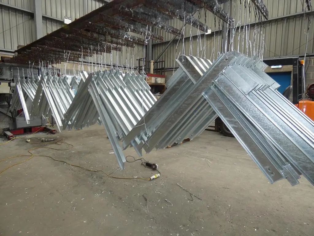 Galvanizlenmiş çelik profillerin sıcak daldırma galvaniz sonrası fabrika ortamında asılı hali — gümüş renkli çinko kaplama
