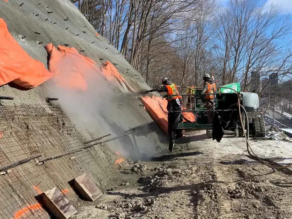 Shotcrete (püskürtme beton) sahada uygulama: işçiler kış koşullarında şev yüzeyine beton püskürtme makinesiyle shotcrete uyguluyor