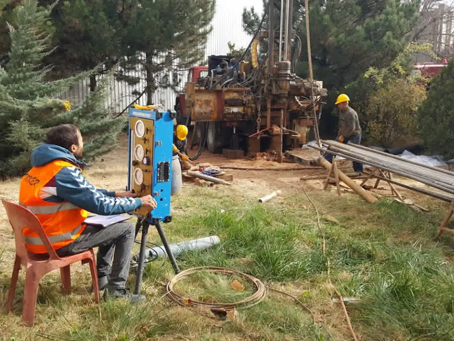 Türkiye'de zemin sondaj calismasi — saha muhendisi kayit defteri tutarken arka planda sondaj makinasi ve isci ekibi gorulmekte; saha koşulları dokumantasyonu ve ekipman guvenligi protokolleri uygulanmakta