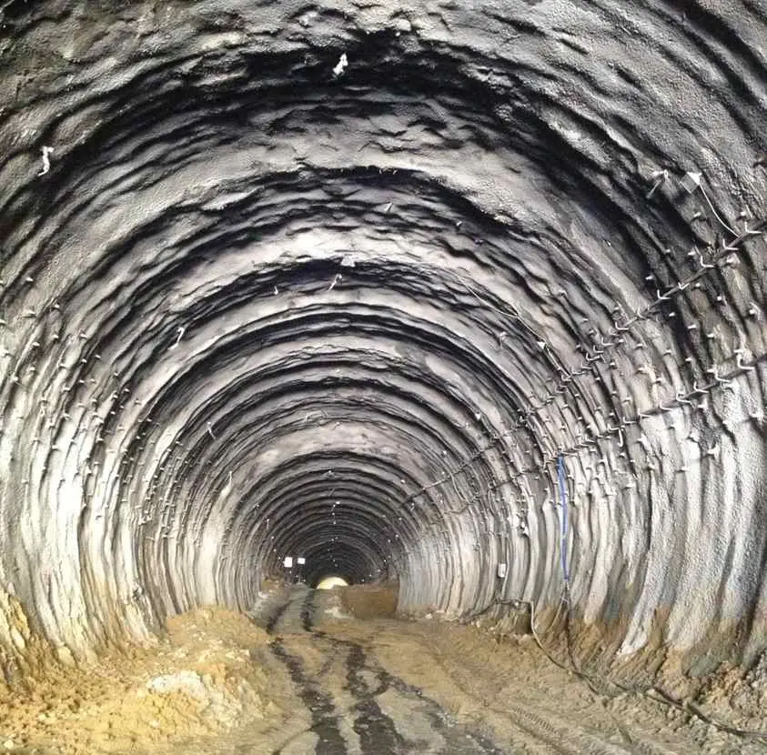 Türkiye kireçtaşı tünelinde doğal kaya tünel içi görünümü — dairesel kesitli düzgün tünel, tavan ve yanlarda tabakalaşmış kireçtaşı süreksizlikleri görünüyor, RMR II–III sınıfı kaya örneği