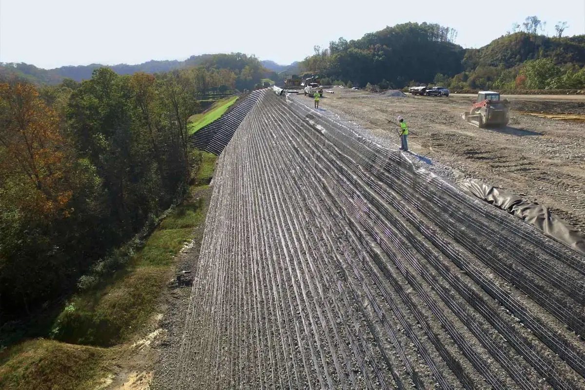 Yol dolgusunda geogrid serme uygulaması — geniş alanda serilmiş geogrid rulolar ve zemin sıkıştırma işlemi