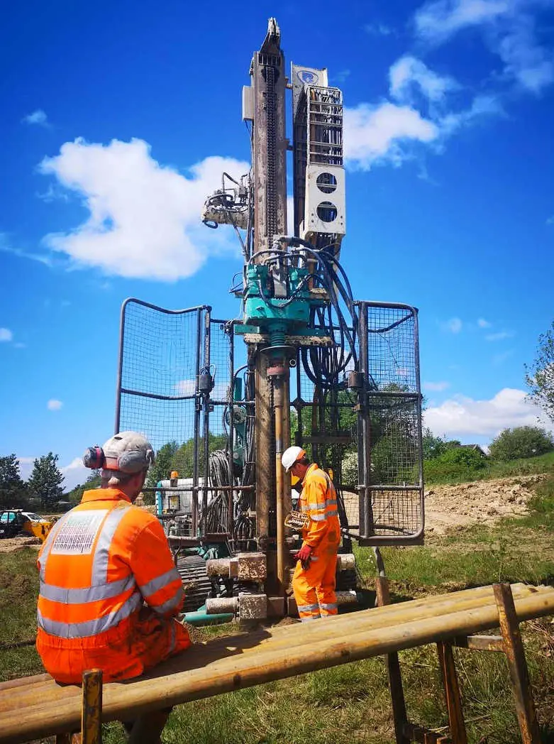 Rotary sondaj makinesi saha uygulaması — iki inşaat mühendisi, yeşil rotary rig, zemin araştırma çalışması