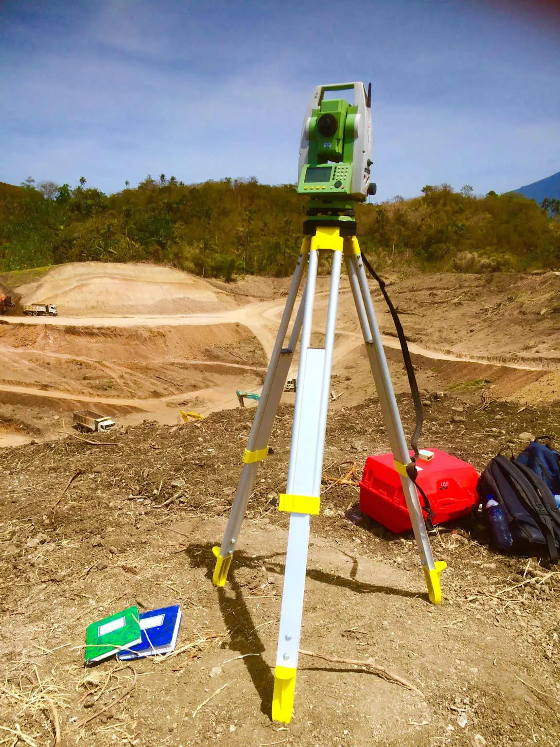 Leica total station şantiye alanında tripod üzerinde kurulu — açık arazi ve kazı çalışmaları arka planda