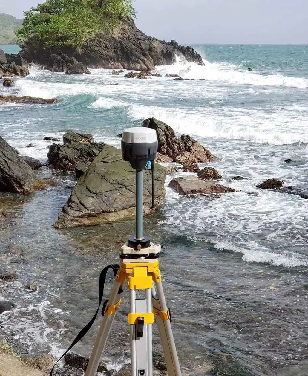 GNSS RTK sabit istasyon alıcısı tripod üzerinde deniz kıyısında kurulu, arka planda kayalık koy ve dalgalı deniz görünmekte