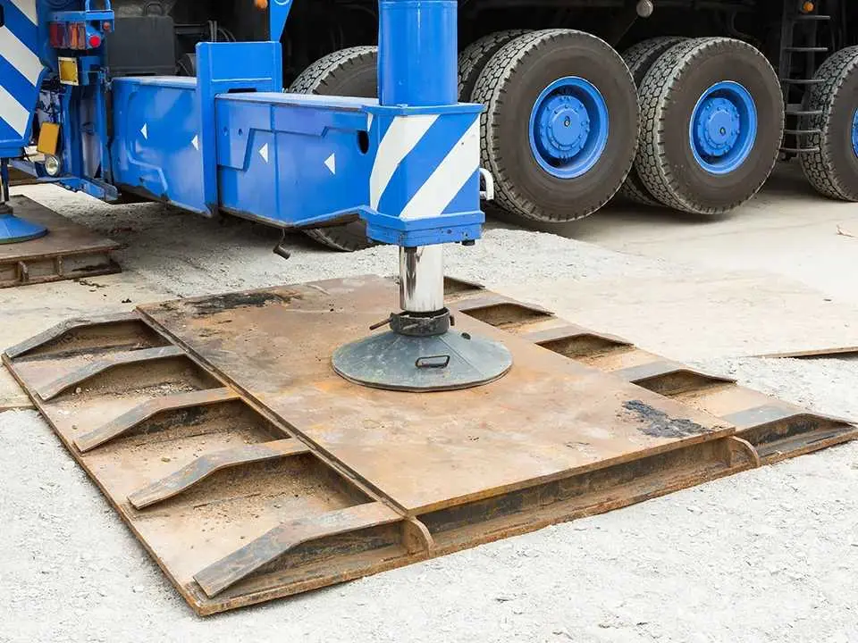 Mavi renkli mobil vincin açılmış destek ayağı (outrigger) ve altındaki büyük çelik zemin plakası; beton zemin üzerinde yük dağıtımı