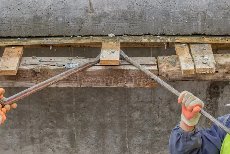 Beton duvar yan kalıp sökme işlemi — işçi levye ile ahşap kalıp çıkarıyor