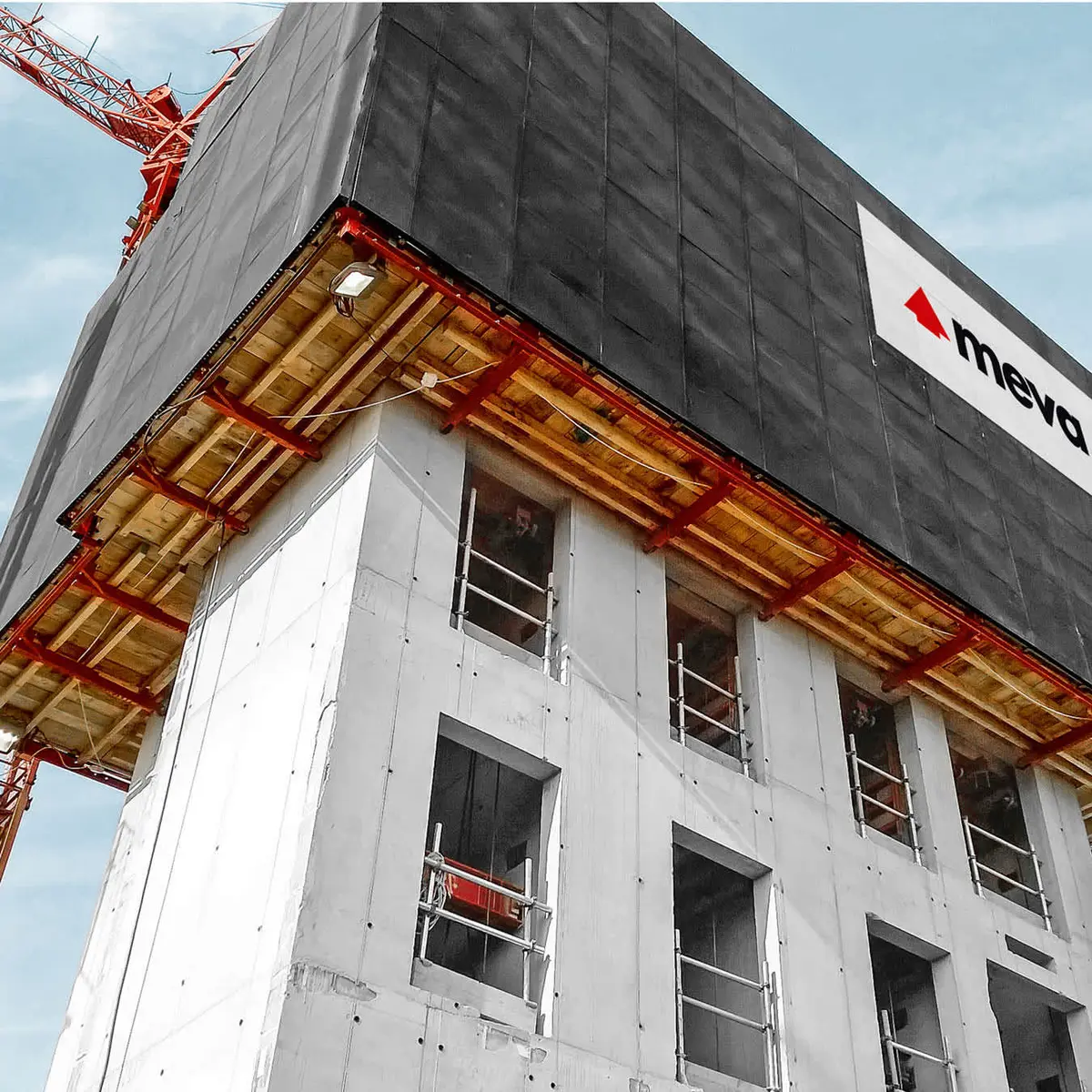 MEVA markalı kendinden tırmanır kalıp sistemi yüksek binanın cephesinde; turuncu çelik konsol yapısı, siyah yüzey paneller ve alt katlarda tamamlanmış beyaz beton görülmekte