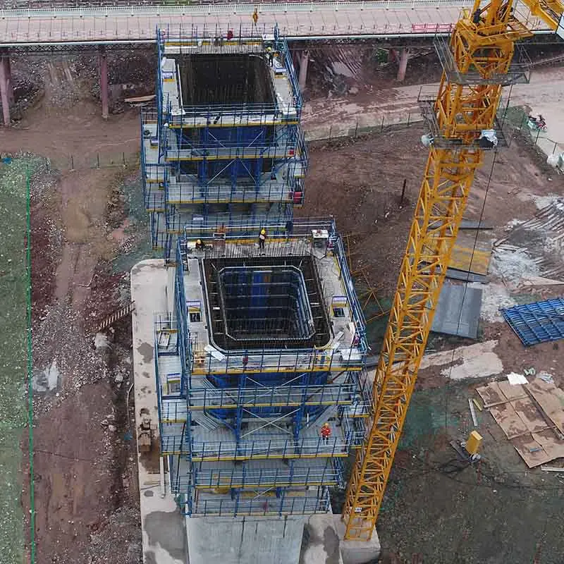 Köprü ayakları inşaatının havadan görünümü; iki ayrı dikdörtgen beton eleman etrafında mavi renkte metal iskele ve tırmanır kalıp sistemi kurulu, şantiye alanı ve sarı vinç görülmekte