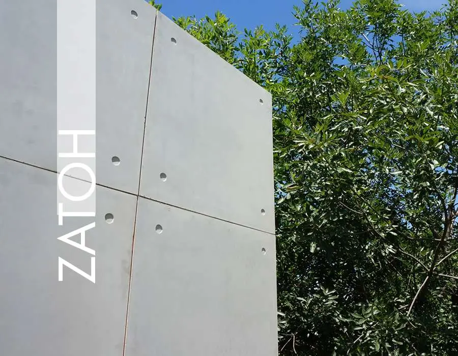 Yeşil ağaçlar önünde düzgün ve temiz gri beton duvar yüzeyi; yatay ve dikey panel ek yerlerinde ankraj delikleri ve ince hatlar görülmekte; ZATOH yazılı marka logosu solda