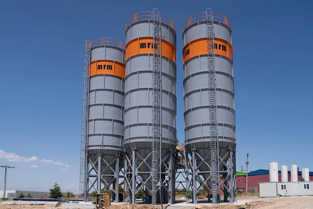 MFM markalı üç gri-turuncu çimento silosu açık alanda sıra halinde — beton santral depolama tesisi