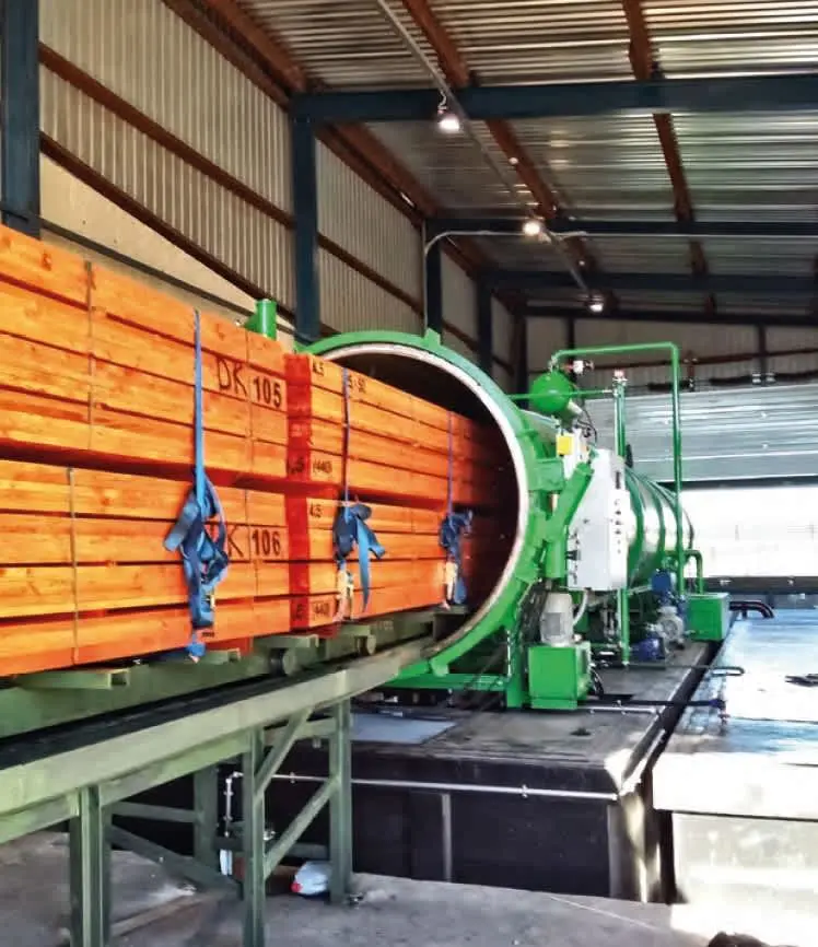 Yeşil otoklav emprenye makinesi ve turuncu lamine ahşap kirişler konveyörde — DK 105 etiketli