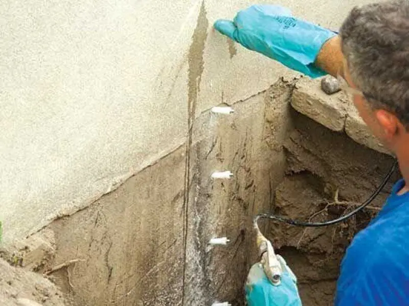 Teknisyen beton temel duvarına kimyasal ankraj enjektörüyle reçine enjeksiyonu yapıyor — çatlak tamiri sahası