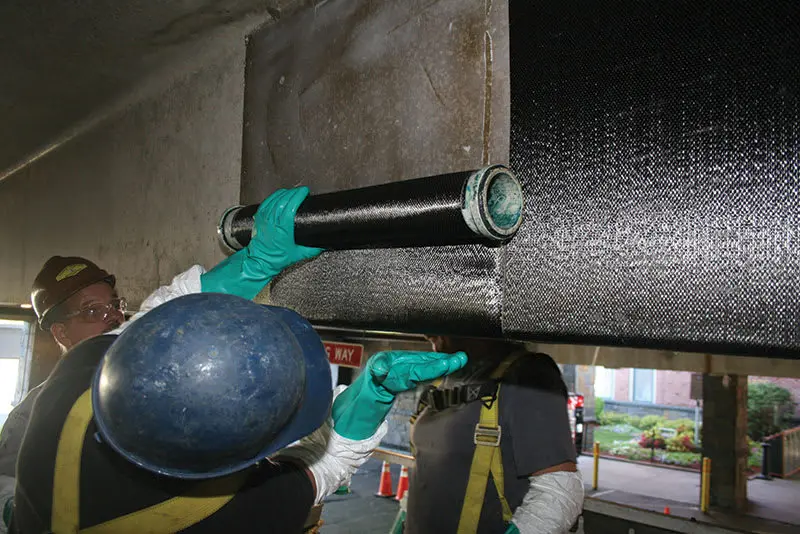 Teknisyenler beton köprü kirişi altına siyah CFRP karbon fiber kumaş rulosu ıslak sargı uygulaması yapıyor