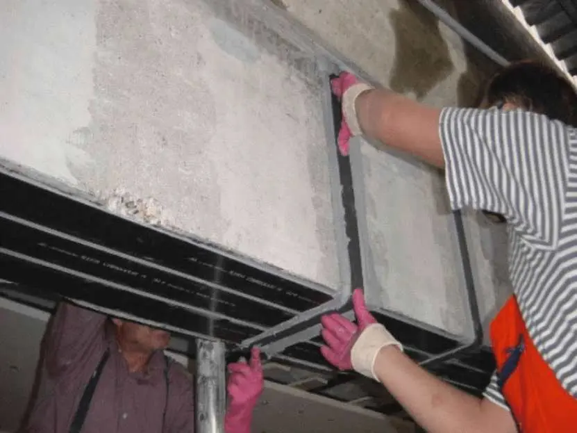 İki teknisyen beton döşemenin alt yüzeyine CFRP karbon fiber laminat plaka yapıştırıyor — eğilme güçlendirmesi