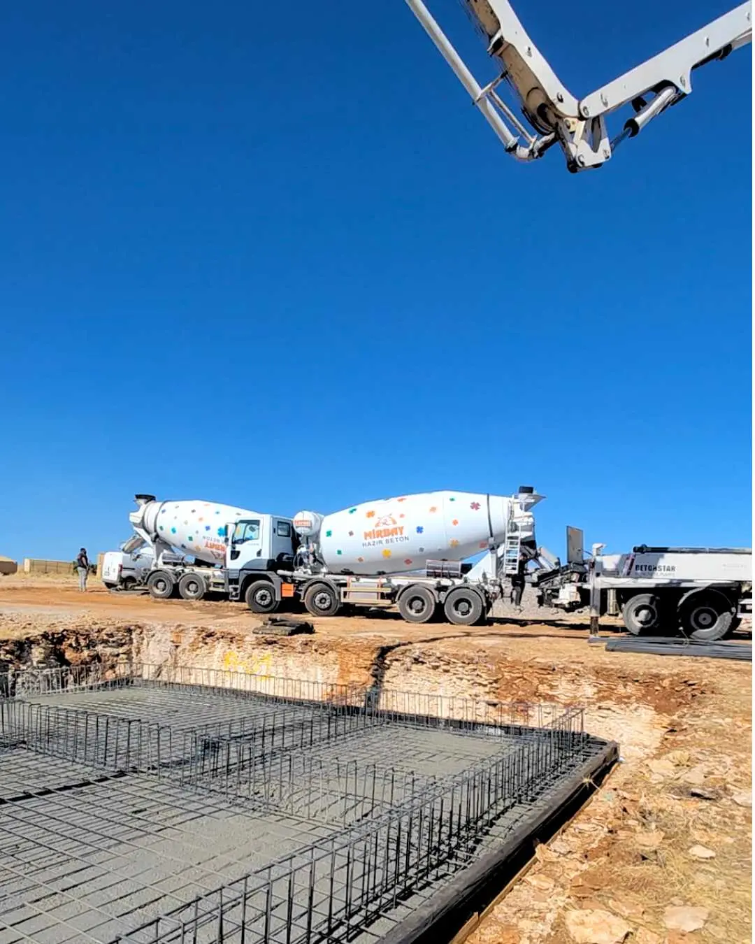 Hazır beton transmikser kamyonları ve pompa bomu ile açık alanda temel beton dökümü sahnesi