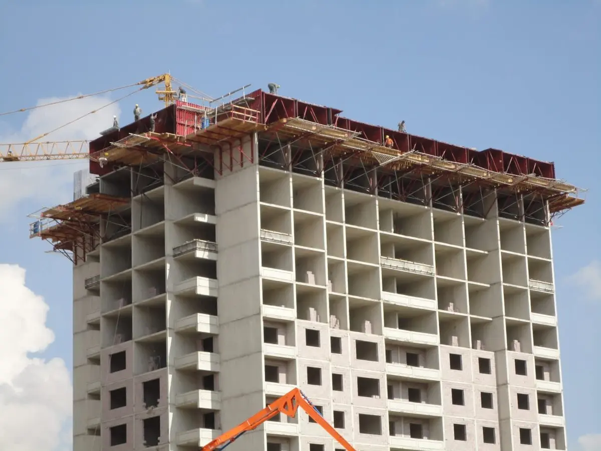 Yüksek katlı betonarme yapı inşaatında tünel kalıp sisteminin en üst kattta kullanımı: kırmızı metal kalıplar vinçle taşınıyor, alttaki katlar tamamlanmış