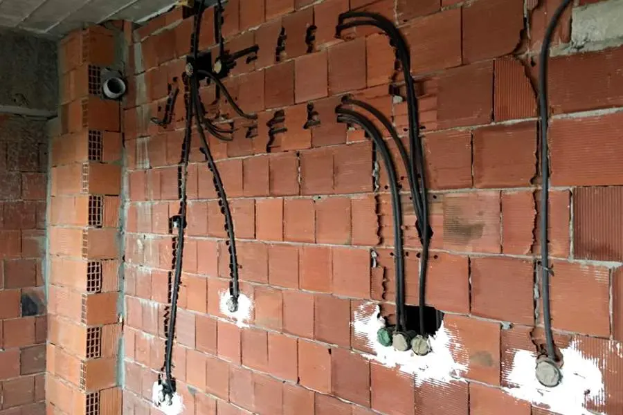 Ham inşaat aşamasında tuğla duvarda gömülü siyah corrugated boru ve elektrik kutuları, kablolar duvara monte bağlantı noktalarından çıkıyor